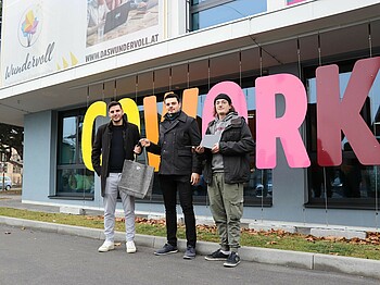 Drei Männer stehen vor einem bunten Schriftzug